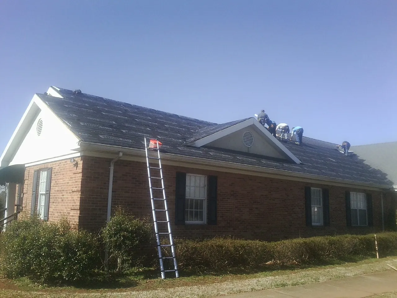 Crew tearing shingles off a brick ranch roof with a ladder set — Metal Roof Repair work by our crew in Pierce