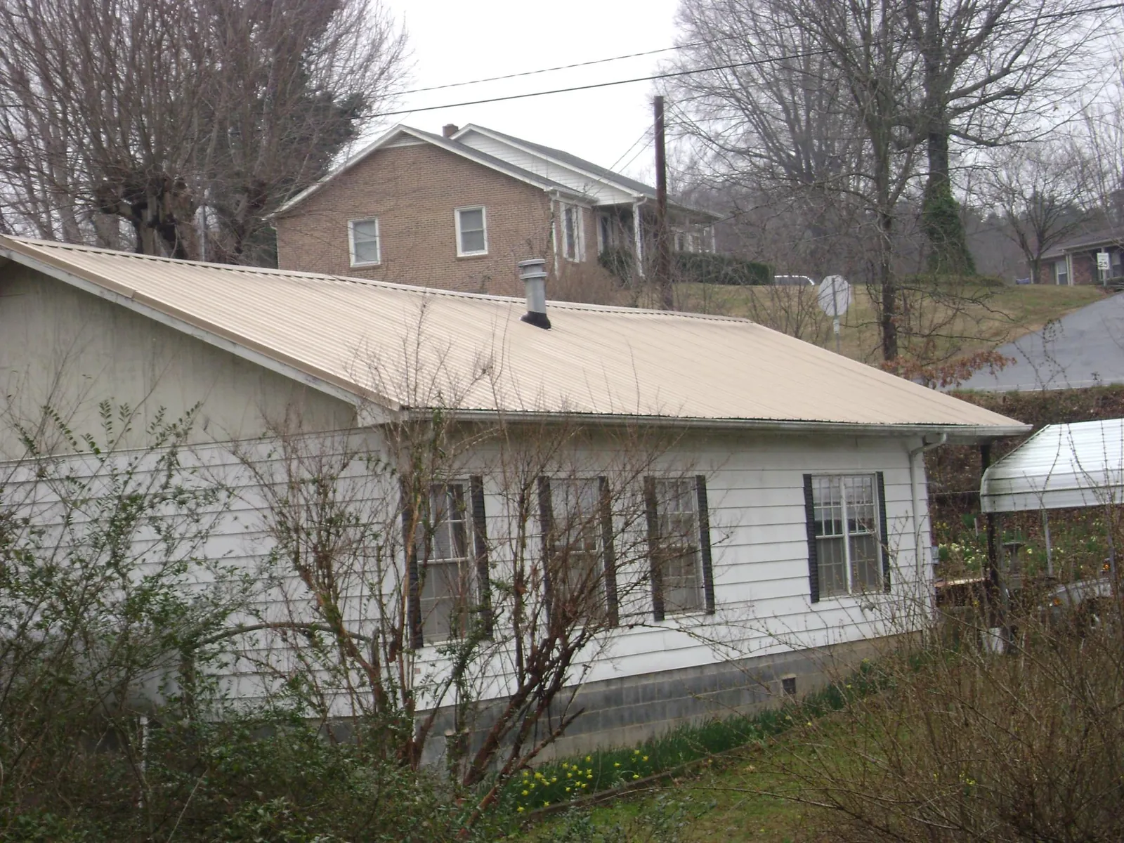 Tan metal roof on a white sided house set into a hillside — Commercial Roofing by Roofing Brothers in Pierce